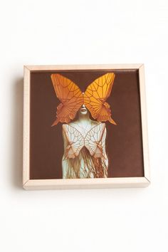 two butterflies sitting on top of a woman's head in a white box with brown background