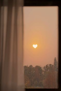 the sun is setting behind a window with trees in the foreground and an overcast sky