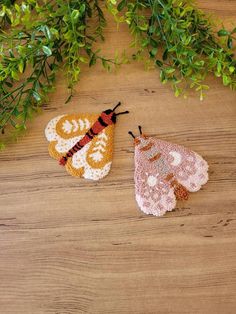 two crocheted bugs sitting on top of a wooden table next to green plants