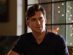 a man sitting at a table in front of a window with christmas lights behind him