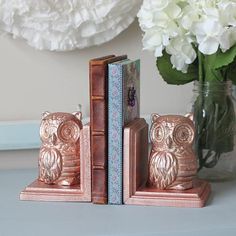 an owl bookend is sitting next to a vase with flowers in it and two books are on the table