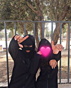 two women in black are standing behind a fence and one has a pink heart on her chest