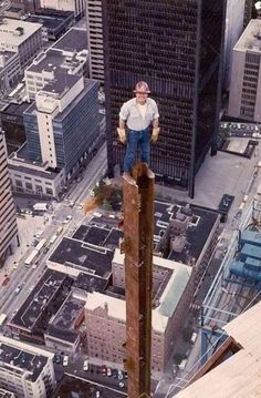 a man standing on top of a tall pole in the middle of a large city