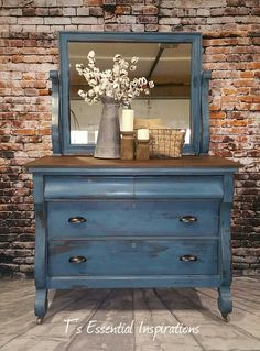 a blue dresser with flowers on top and a mirror in the middle, against a brick wall