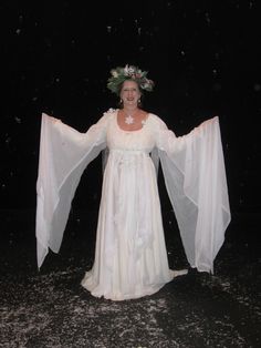 a woman in a white dress is standing with her arms spread out and wearing a flower crown