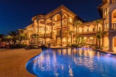 a large mansion with a swimming pool in the middle of it at night, surrounded by palm trees