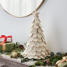 a white christmas tree sitting on top of a wooden table next to presents and a round mirror