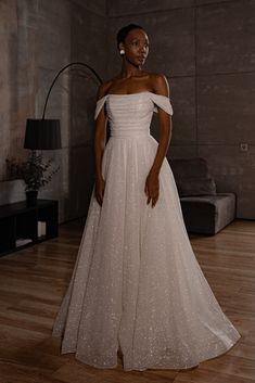 a woman in a white dress standing on a wooden floor with her hand on her hip