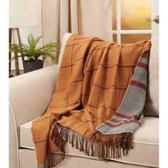 an orange and grey plaid blanket sitting on top of a couch next to a potted plant