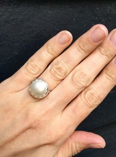 Choose your color and your ring size! This elegant and stately pearl ring is made from a beautiful and unique white cream 14mm Mabe South Sea AAA Pearl that has many hues including pink. The pearl has been set in sterling silver with a sterling silver ring band handmade from half dome wire. This ring has some height, the setting is almost 1/2 inch high. The white cream pearl is more matte than the other mabe pearls listed, but still has a luminescent quality that makes it captivating!Made to ord Classic White Pearl Ring With Pearl Charm, Classic White Pearl Ring With Charm, Classic White Pearl Ring With Drop Detail, Elegant White Pearl Ring With Charm, Classic White Pearl Ring, Elegant White Moonstone Round Ring, Elegant White Round Moonstone Ring, White Pearl Drop Ring For Anniversary, Elegant White Moonstone Ring