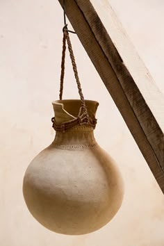 a white vase hanging from a wooden beam with rope attached to the top and bottom