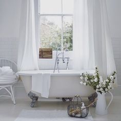 a white bath tub sitting under a window next to a vase with flowers in it