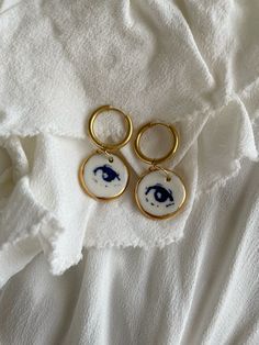 two gold hoop earrings with blue and white designs hanging from them on a white towel