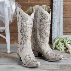 a pair of white cowboy boots sitting on top of a wooden floor next to flowers