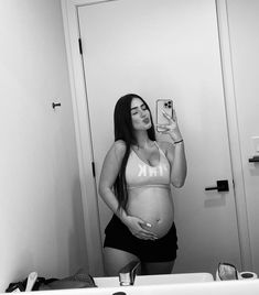 a pregnant woman taking a selfie in front of a bathroom mirror with her cell phone