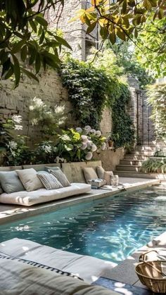 an outdoor swimming pool surrounded by greenery and stone walls, with lounge chairs in the foreground