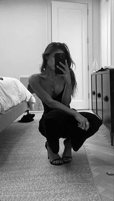 a woman kneeling on the floor taking a selfie with her cell phone in a bedroom