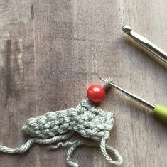 the crochet hook is being worked on with two knitting needles and an orange ball of yarn