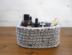 a crocheted basket with bottles and hairbrushes in it on a wooden table