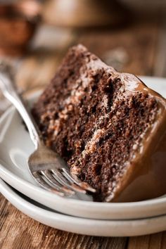 a slice of chocolate cake on a white plate with a fork next to the rest of the cake