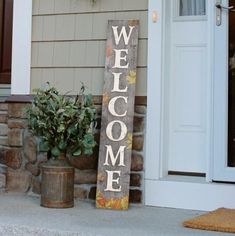 a welcome sign sitting on the side of a house next to a potted plant