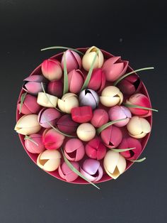 tulips and other flowers in a bowl on a black surface with green stems