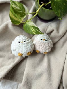 two small white sheep sitting on top of a bed next to a potted plant