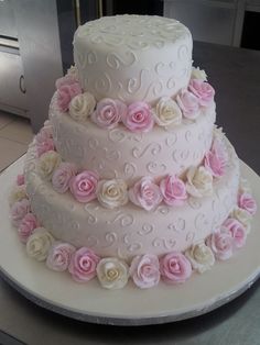 a three tiered wedding cake with pink and white flowers on the bottom, sitting on a table