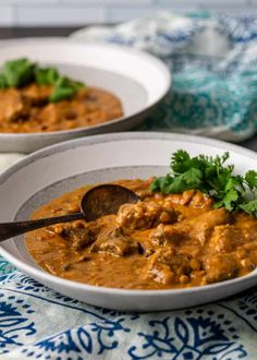 two white bowls filled with curry and garnished with cilantro leaves on top