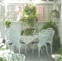 an outdoor table and chairs with potted plants on the back deck, surrounded by greenery