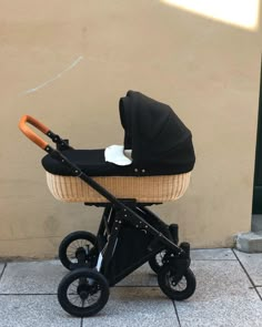 a black stroller with an orange handlebar on the sidewalk next to a wall