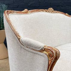 an ornately decorated chair in front of a blue brick wall and potted plant