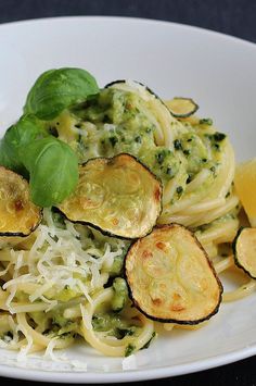 pasta with zucchini and spinach on a white plate next to lemon wedges