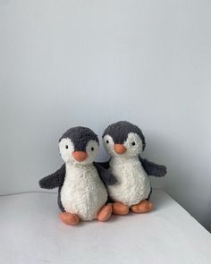 two small stuffed penguins sitting on top of a white table next to each other,