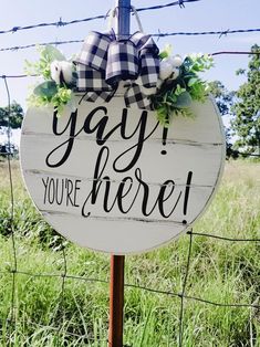 a sign that says yay you're here hanging on a fence post in the grass