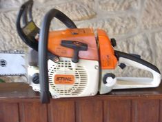 an orange and white chainsaw sitting on top of a wooden table