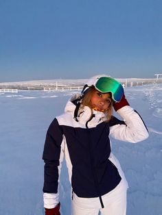 a woman standing in the snow with skis on her head and goggles on