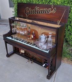 an old piano with liquor bottles and glasses sitting on it's stand in front of a bush