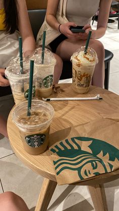 two women sitting at a table with starbucks drinks on it and one holding a cell phone