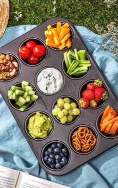 a muffin tin filled with different types of fruits and vegetables next to an open book