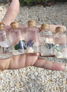 small bottles filled with different types of sea glass and sand in the palm of someone's hand