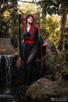 a woman with red hair is sitting on a chair in the woods next to a waterfall