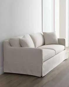 a white couch sitting on top of a hard wood floor next to a tall window