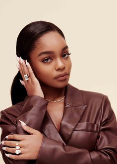 a woman in a brown leather jacket holding her hand to her face and looking at the camera