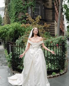 a woman in a wedding dress is standing on the sidewalk with her arms outstretched out