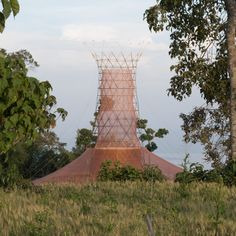 a large structure sitting on top of a lush green field next to trees and tall grass