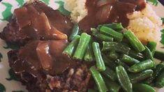 a plate topped with meat, gravy and green beans next to mashed potatoes