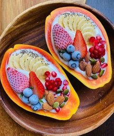 two halves of fruit with nuts and berries in them on a wooden plate next to a spoon