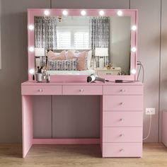 a pink vanity with lights on it and a bed in the background