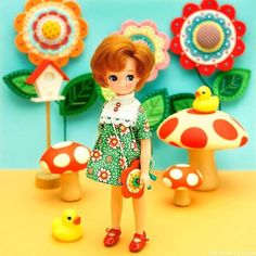 there is a doll standing next to mushrooms and flowers